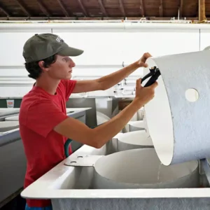 An oyster hatchery worker does maintenance on part of a holding tank.